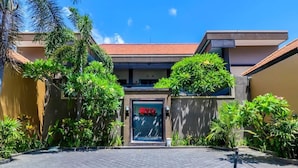 A modern building with a tiled roof, a central entrance with a glass door, and surrounding greenery. - OYO 2143 Leluhur Bali Apartment (Keroboken Kelod)