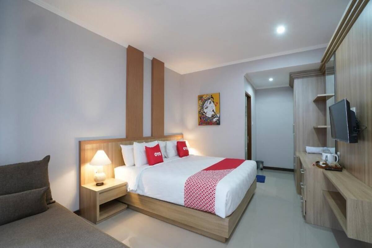 A hotel room with a bed, bedside table, lamp, TV, and a small desk area.