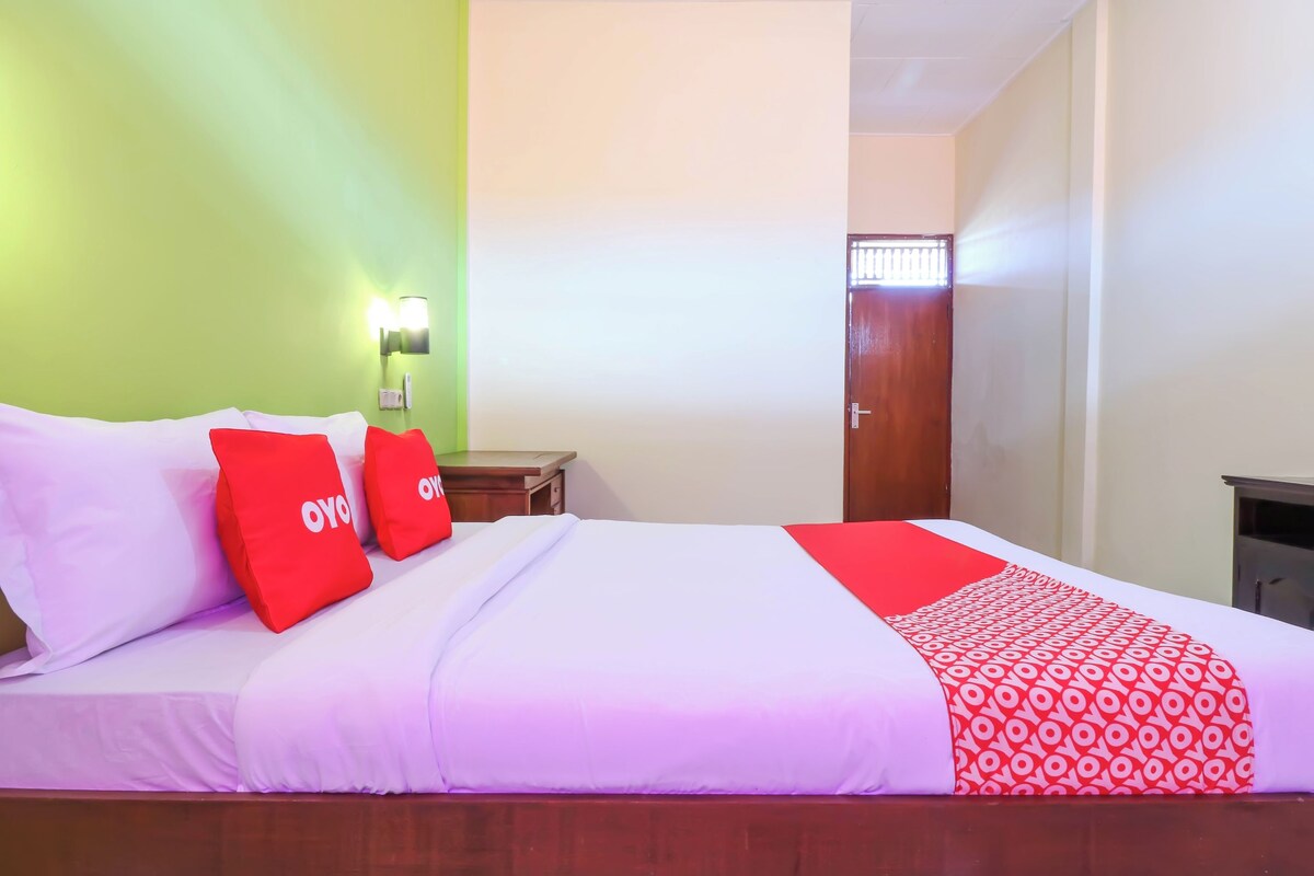 A hotel room with a bed, pillows, a nightstand, a lamp, and a door.