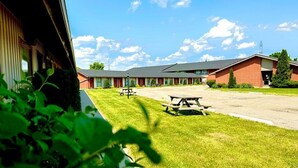 A motel with a parking lot, picnic tables, and a grassy area. - Festival Courtyard Inn (Stratford)