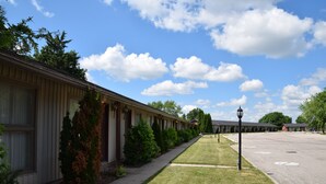 A row of motel-style buildings with a paved walkway and a grassy area in front. - Festival Courtyard Inn (Stratford)