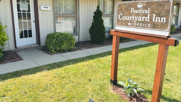 A sign for Festival Courtyard Inn with a wooden post, a door, and a small sign indicating the office location. - Festival Courtyard Inn (Stratford)