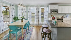 Een keuken met een houten tafel, blauwgroene stoelen, een kleurrijk vloerkleed en witte kastjes.