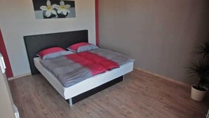 A bedroom with a bed, a nightstand, a potted plant, and a wall-mounted picture. - Apartment 3 - Jack & Richies apartments (Greifswald)