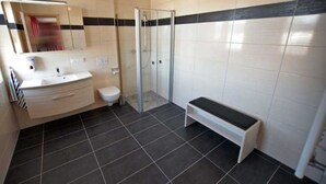 A modern bathroom with a glass shower enclosure, a white sink, and a bench. - Apartment 3 - Jack & Richies apartments (Greifswald)