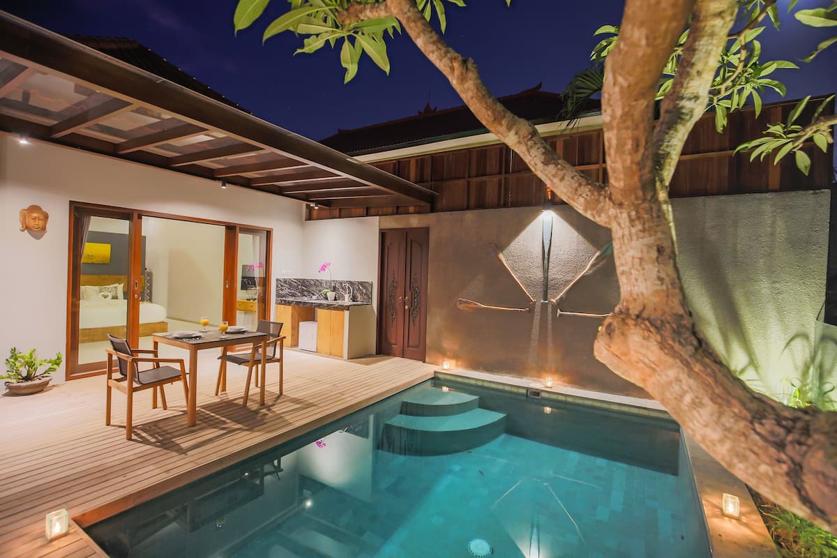 A modern outdoor pool area with a wooden deck, a dining table, and chairs.