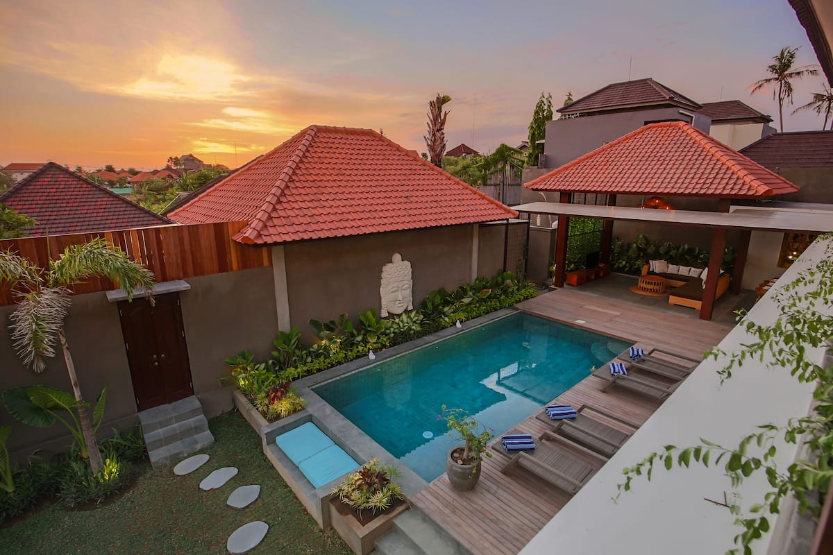 A pool area with a wooden deck, lounge chairs, and a statue.