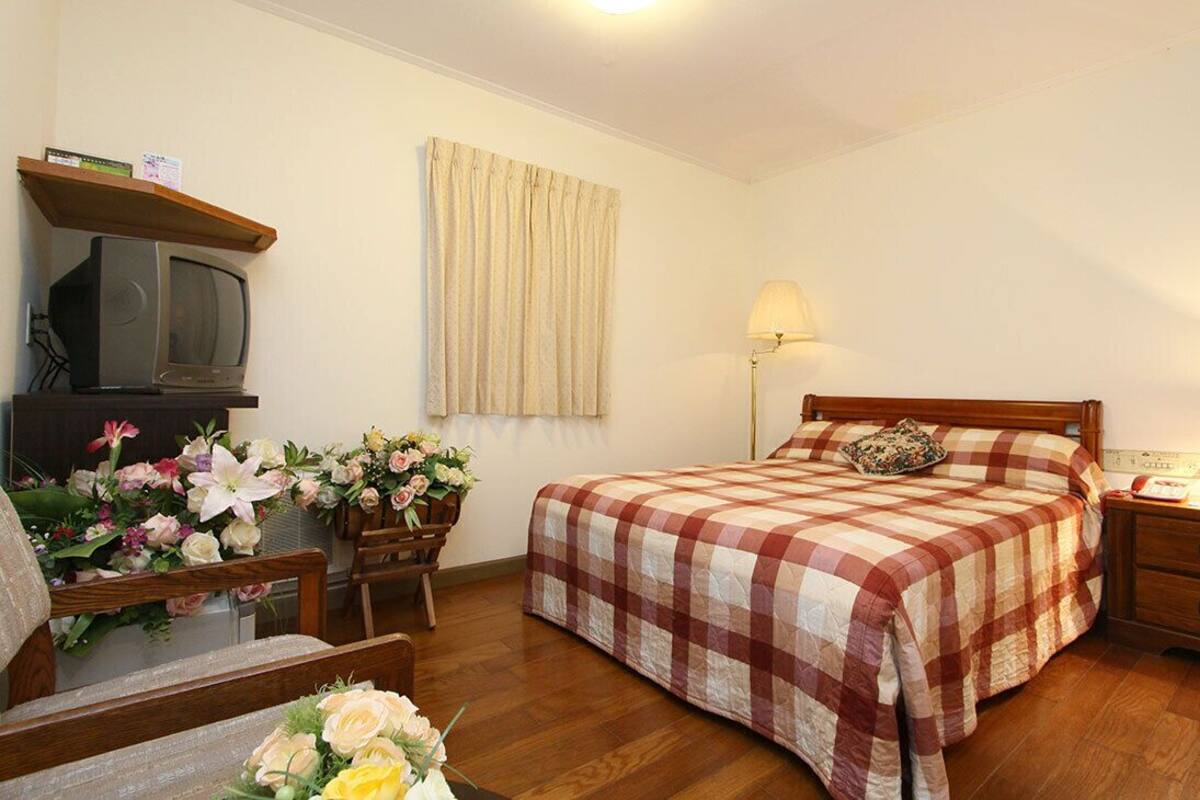 A bedroom with a bed, bedside table, lamp, and a television on a shelf.