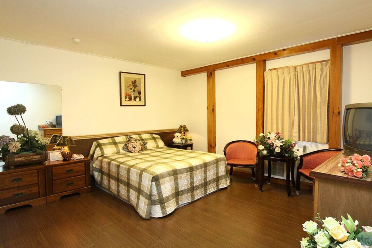 A bedroom with a bed, a desk with a television, a chair, a nightstand, and a dresser.
