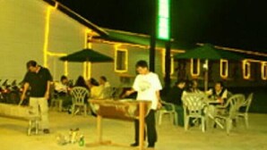 An outdoor seating area with tables and chairs, a green umbrella, and bicycles parked nearby.
