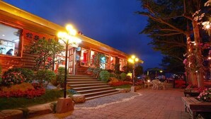 A restaurant with outdoor seating, illuminated by warm lights, and surrounded by landscaped gardens.