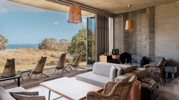 A modern living room with a large glass door leading to an outdoor area, wicker furniture, and a grey sofa. - Wandering Walls (Hengchun)