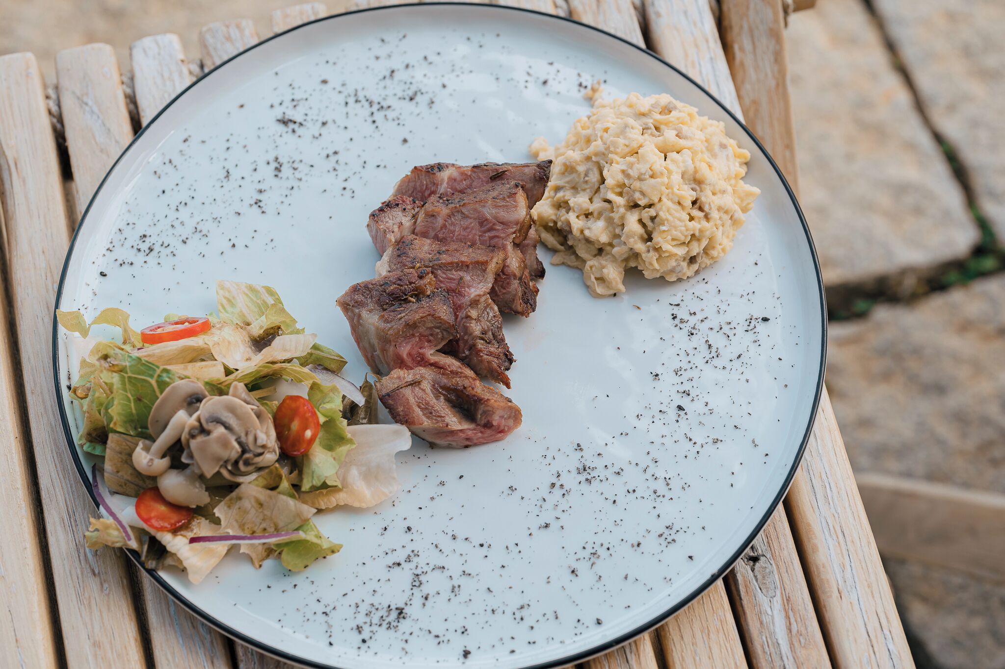 A plate with grilled meat, mashed potatoes, and a salad on a wooden table.