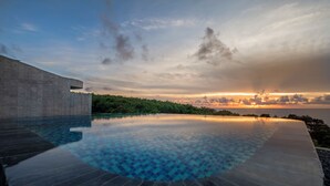 An infinity pool with a clear view of the sunset over the ocean, surrounded by lush greenery and a modern building structure. - Wandering Walls (Hengchun)