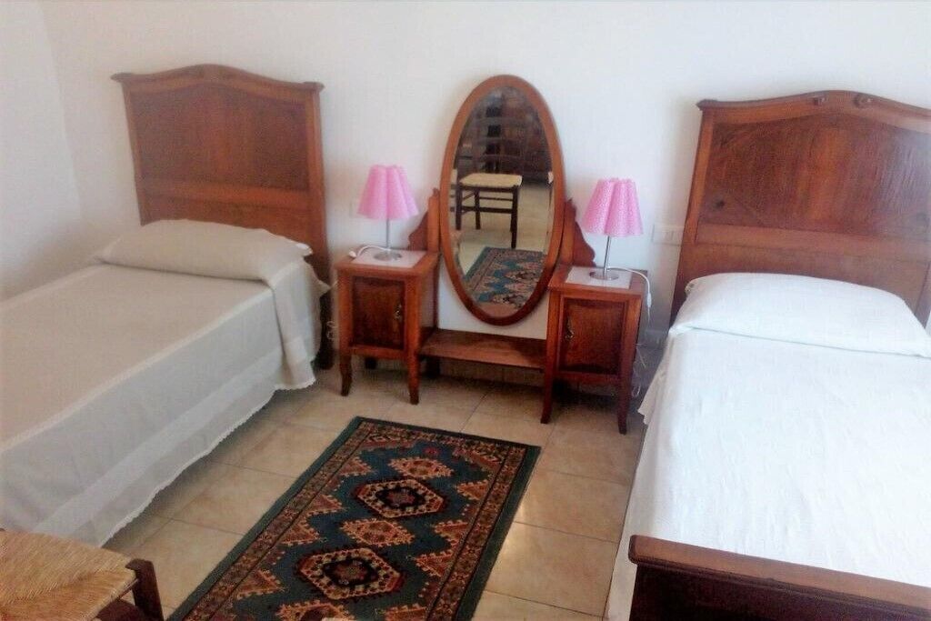 A bedroom with two single beds, a wooden headboard, a mirror, and a small table with a lamp.