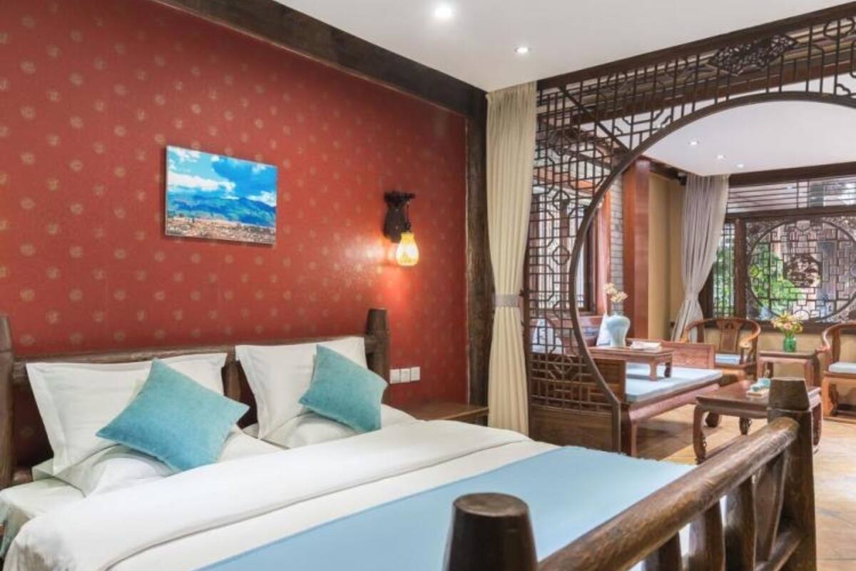 Habitación de hotel con cama, cabecera de madera, luz de pared y vista al área de estar exterior.