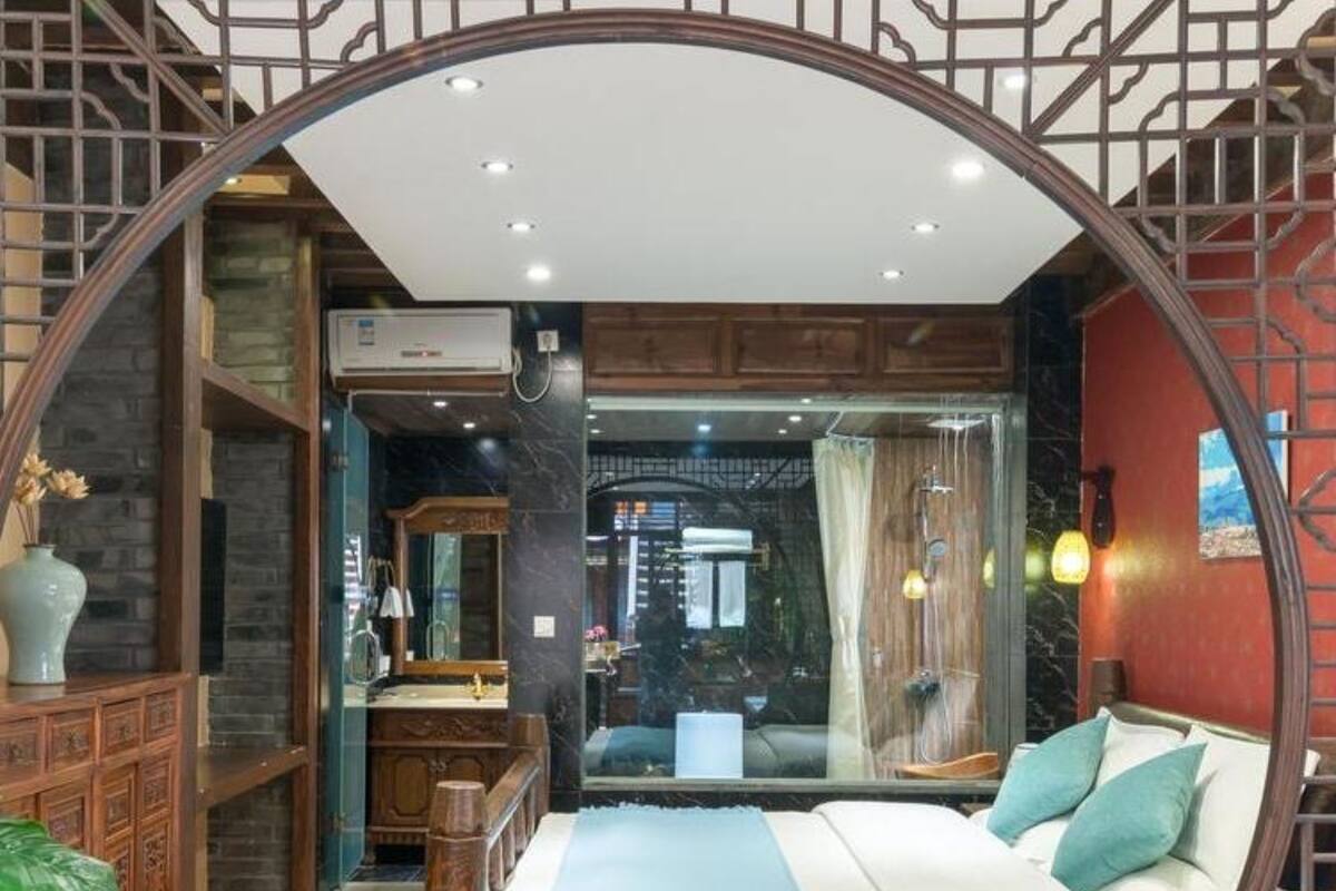 Un dormitorio con un arco circular, una cama con una manta azul, un aparador de madera y un baño visible a través de una puerta de vidrio.