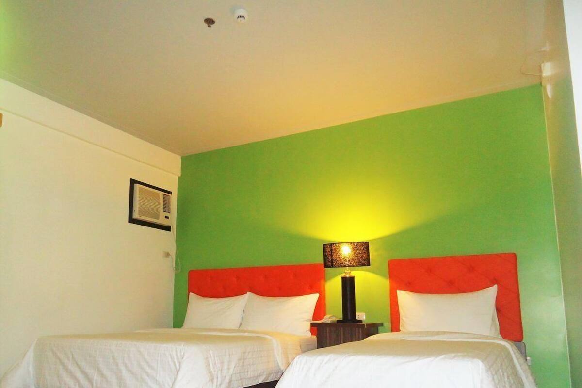 Een hotelkamer met twee bedden, elk met wit beddengoed en rode hoofdborden. Daartussen staat een nachtkastje met een lamp.
