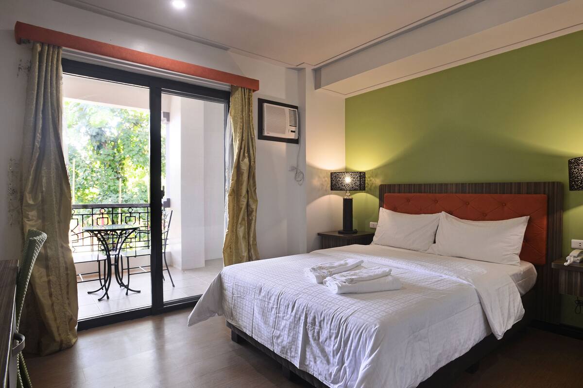 Een hotelkamer met een bed, twee bedlampen, een groene wand en een balkon met een tafel en stoelen.