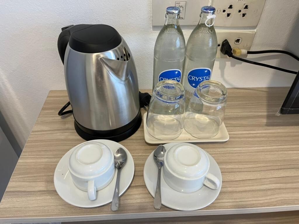 A kitchen counter with a kettle, two bottles of Crystal water, and two sets of cups and spoons.
