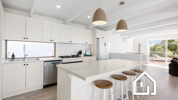 Una cocina moderna con armarios blancos, una isla central con taburetes e iluminación colgante.