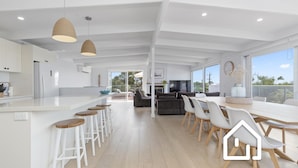 Una cocina moderna con una isla central, taburetes de bar y un comedor con una mesa grande y sillas.