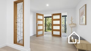 Un interior espacioso con puertas de madera que dan a un balcón, un pequeño banco de madera y un cuadro enmarcado en la pared.