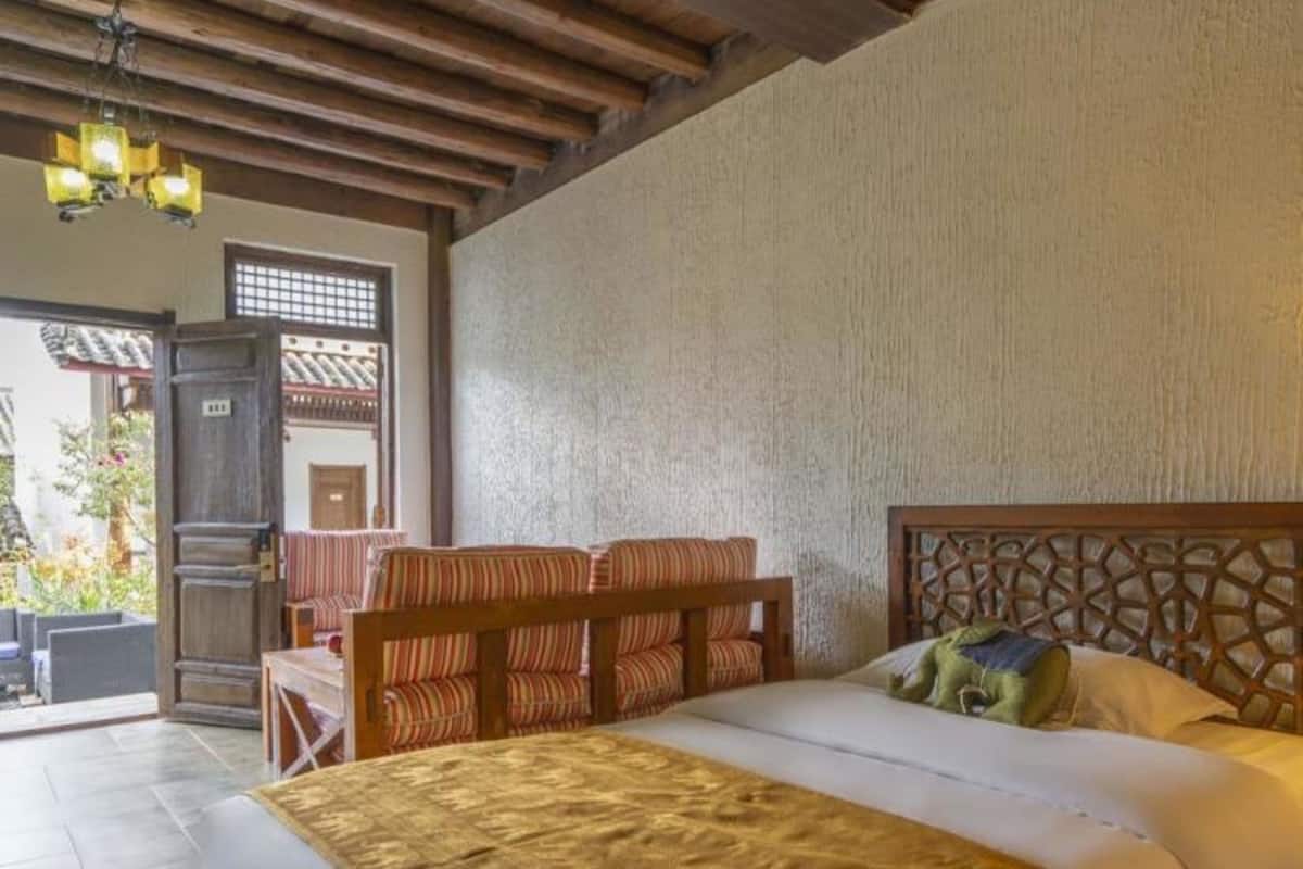 A bedroom with a wooden headboard, a bed with a gold cover, and a wooden bench with striped cushions.