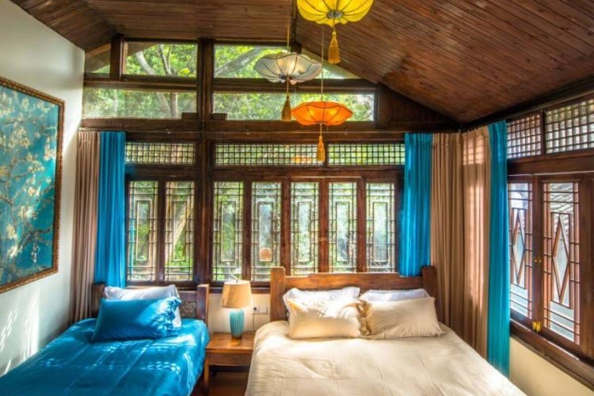 A traditional room with wooden beams, two beds with blue and white bedding, and a large window with blue curtains.