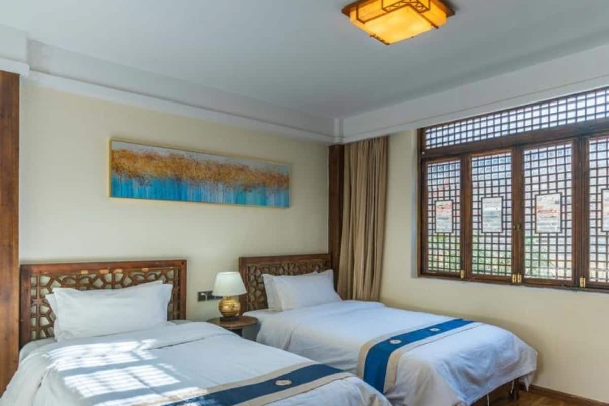 A room with two beds, a painting on the wall, a window with a view, and a ceiling light.