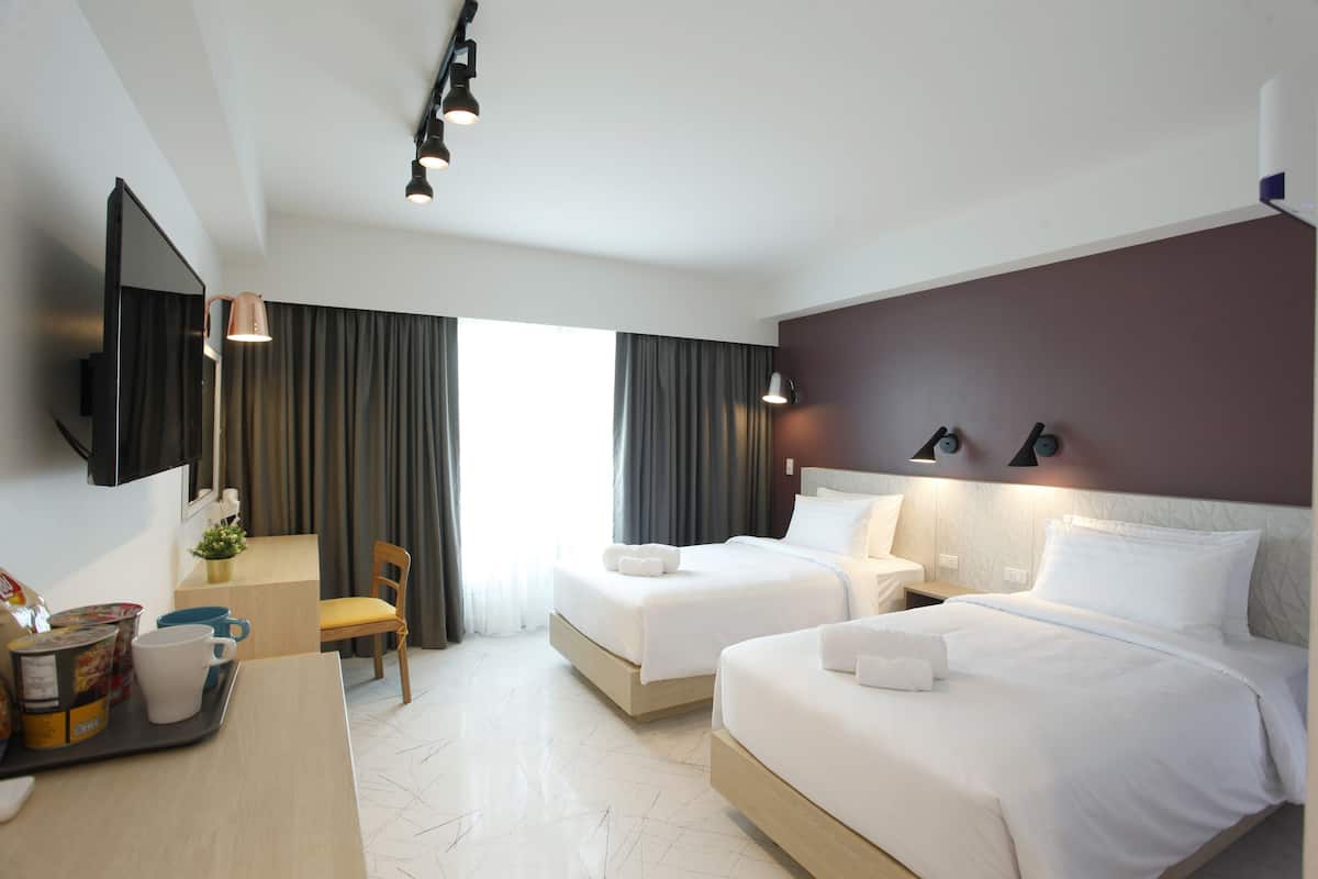 A hotel room with two beds, a desk, a chair, a TV, and a window with curtains.