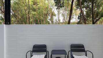 Two black metal chairs with white cushions against a white wall, with a view of trees in the background.