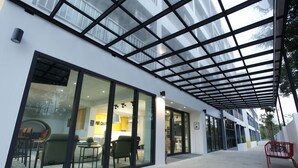A modern building with large glass windows, a covered outdoor area, and a visible interior with furniture. - Port Canary Hotel (Bangkok)