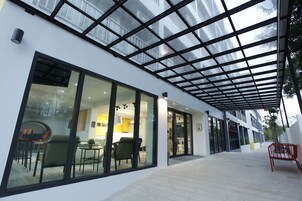 Ένα σύγχρονο κτίριο με μεγάλα παράθυρα από γυαλί, έναν σκεπαστό εξωτερικό χώρο και έναν εσωτερικό χώρο με έπιπλα που είναι ορατός από έξω.