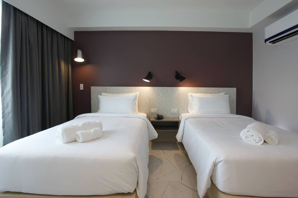 A hotel room with two beds, each with white linens and towels, a marble headboard, and a dark brown accent wall.