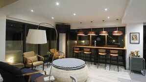 A modern living room with a round ottoman, a large floor lamp, and a dining area with bar stools. - Port Canary Hotel (Bangkok)