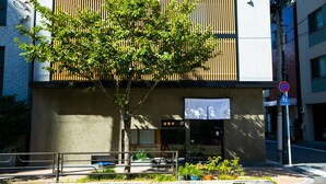 Un bâtiment avec un arbre devant, une enseigne avec des caractères japonais et un panneau indiquant qu’il est interdit de se garer.
