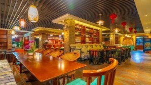 A restaurant with wooden tables and chairs, a bar area, and a bookshelf.