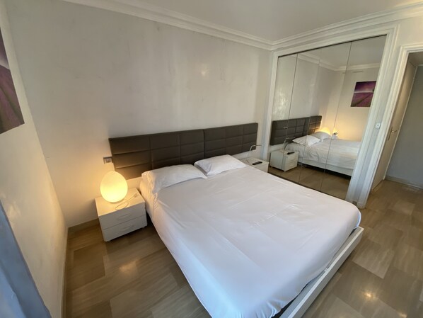 A modern hotel room with a large bed, a bedside table with a lamp, and a mirror on the wall. - One Bedroom - Rue D'Antibes (Cannes)