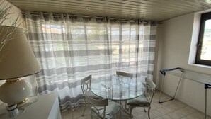 A dining area with a glass table and metal chairs, a white lamp, and a window with a view of buildings. - One Bedroom - Rue D'Antibes (Cannes)