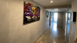 A hallway with a large abstract painting on the wall, a mirror, and a door leading to another room. - One Bedroom - Rue D'Antibes (Cannes)