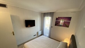 A bedroom with a bed, a television mounted on the wall, a window with curtains, and a picture on the wall. - One Bedroom - Rue D'Antibes (Cannes)