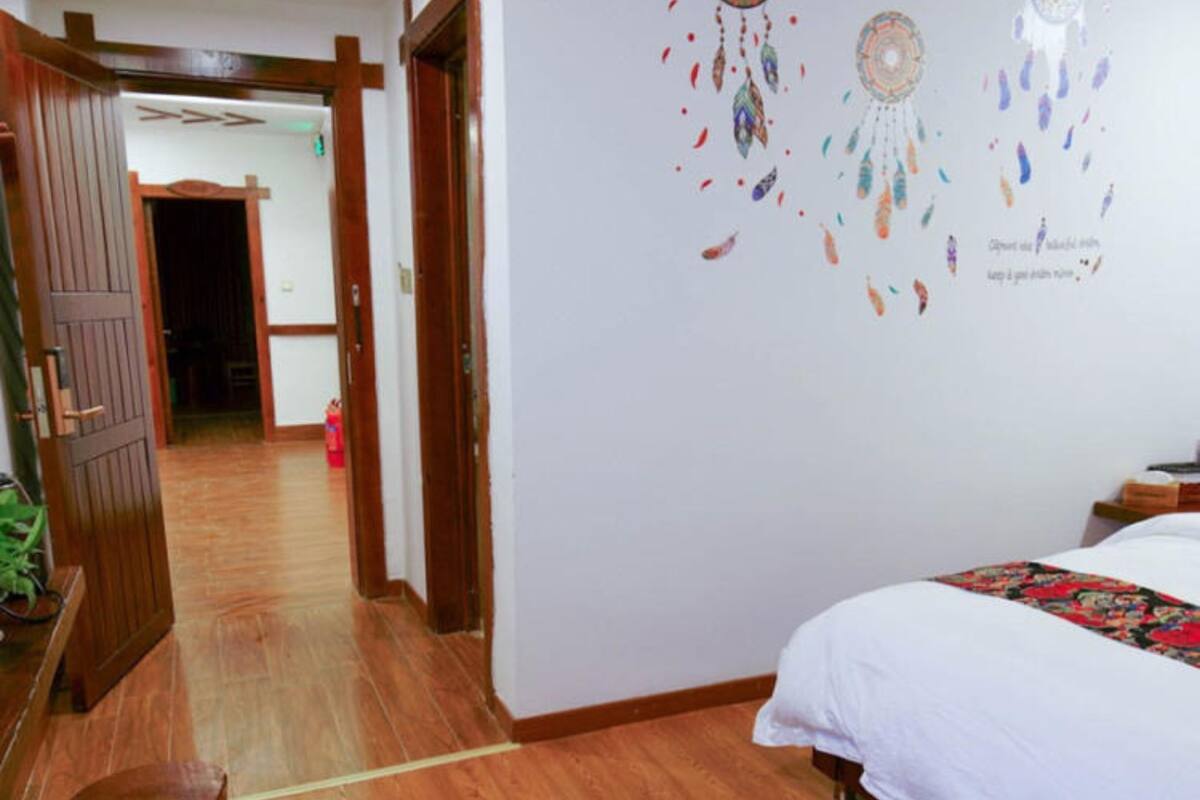 A hotel room with a wooden floor, a bed with white bedding, a wooden door, and a wall with dreamcatchers.