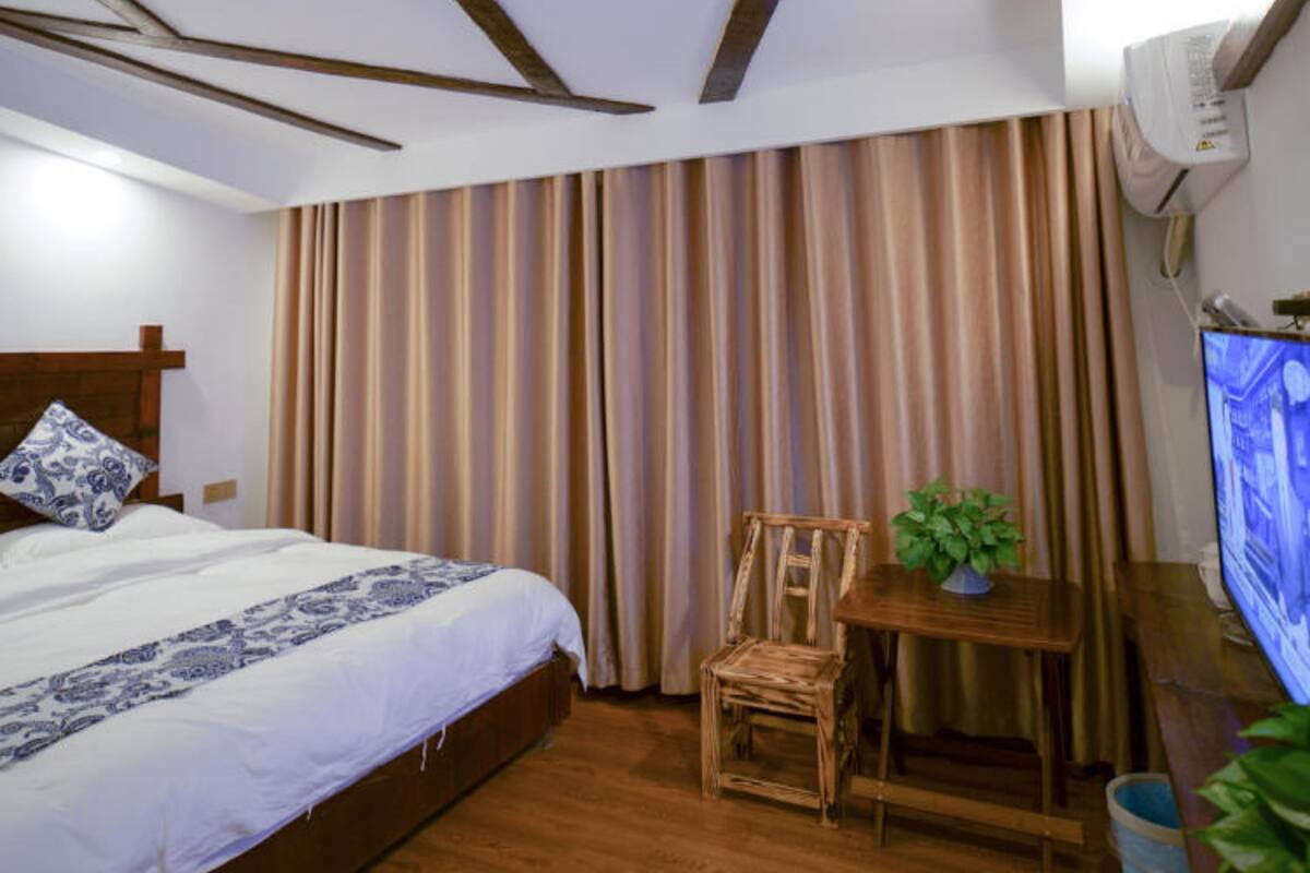 A hotel room with a bed, a wooden chair, a small table with a plant, and a television.