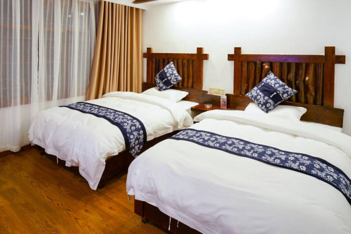 A room with two beds, wooden beams on the ceiling, and a window with sheer curtains.