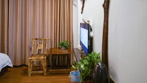 A hotel room with a wooden bed, a wooden chair, a small table with a plant, a television, and a wall-mounted air conditioner. - Floral Hotel · Spring Guesthouse Zhangjiajie (Zhangjiajie)