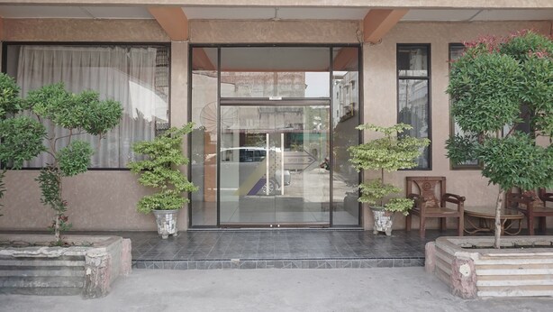 L’entrée d’un hôtel avec une porte en verre, des plantes en pot et des sièges à l’extérieur.