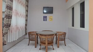 Un petit coin repas avec une table ronde et quatre chaises en bois, un rideau à motifs et deux panneaux accrochés au mur.