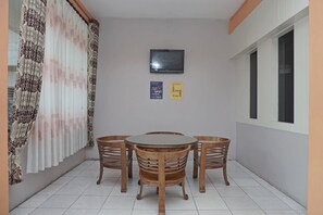 Un petit coin repas avec une table ronde et quatre chaises en bois, un rideau à motifs et deux panneaux accrochés au mur.