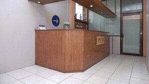 Un comptoir d'accueil avec une pancarte indiquant « SDT ON », situé dans un hall d'entrée moderne doté d'un sol carrelé et d'une porte en verre en arrière-plan.